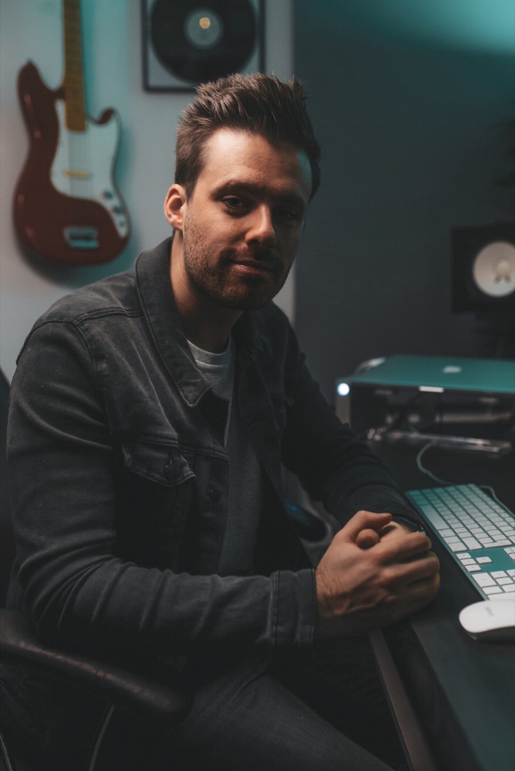 Ed Stokes sitting at his desk in the studio, guitar on the wall behind him